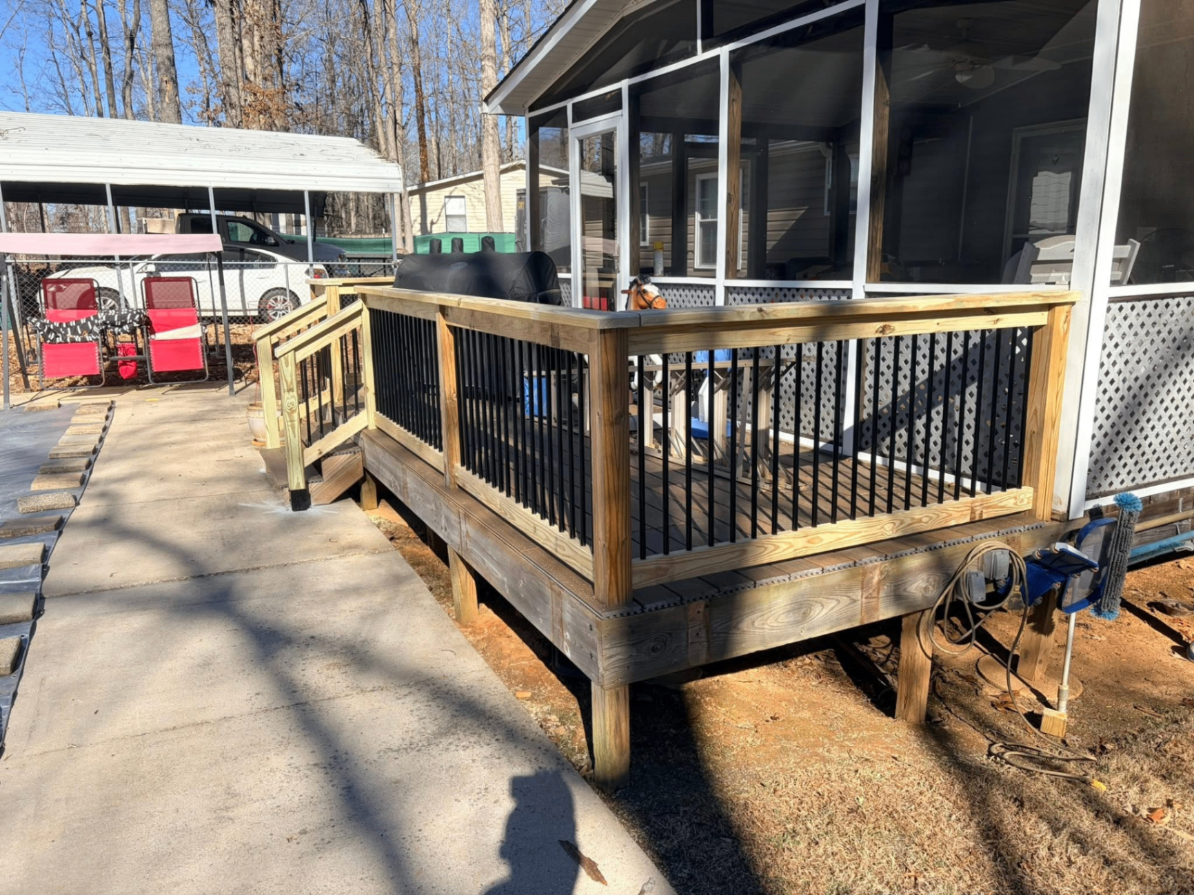 Wood deck with black metal balusters attached to a screened porch with side ramp